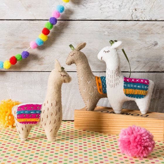 Corinne Lapierre Felt Llamas Craft Kit. A colourful scene. There are 3 Llamas. All three Llamas are wearing multi coloured waistcoats. 