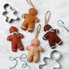 A white floured background. there are four felt gingerbread men in shades of caramel, beige and brown and two silver cookie cutters.