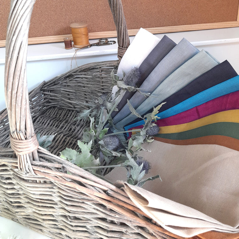 A basket of linen squares and flowers. Cotton thread reels and scissors are in the back ground.