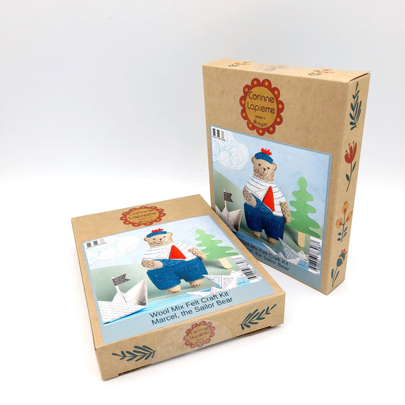 Corinne Lapierre Felt Craft Mini Kit. A bear is stood, wearing a white t shirt with blue stripes.dark blue trousers and hat. The hat has a red pom pom. He is holding a toy sailing boat.