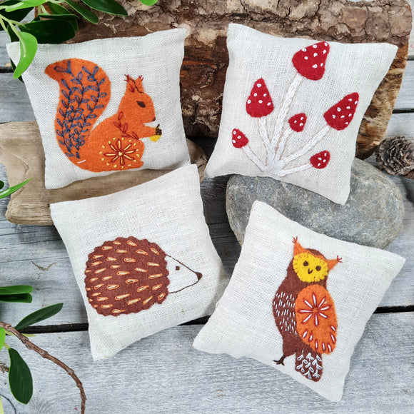 Corinne Lapierre Linen Lavender Bags Embroidery Kit. Image of 4 light beige linen lavender bags, depicting an owl, red squirrel, hedgehog and toadstools.